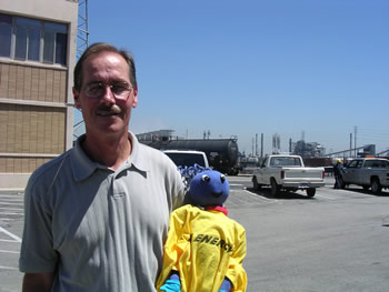 Image of Enegy Ant, wearing a souvenir, and friend outside of Carson Refinery