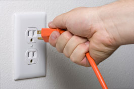 A photo of a person's hand unplugging an electrical appliance cord from an electricity outlet